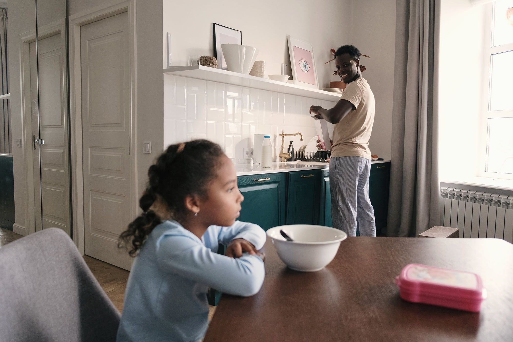 Une fillette attend son petit-déjeuner pendant que son père prépare le repas.