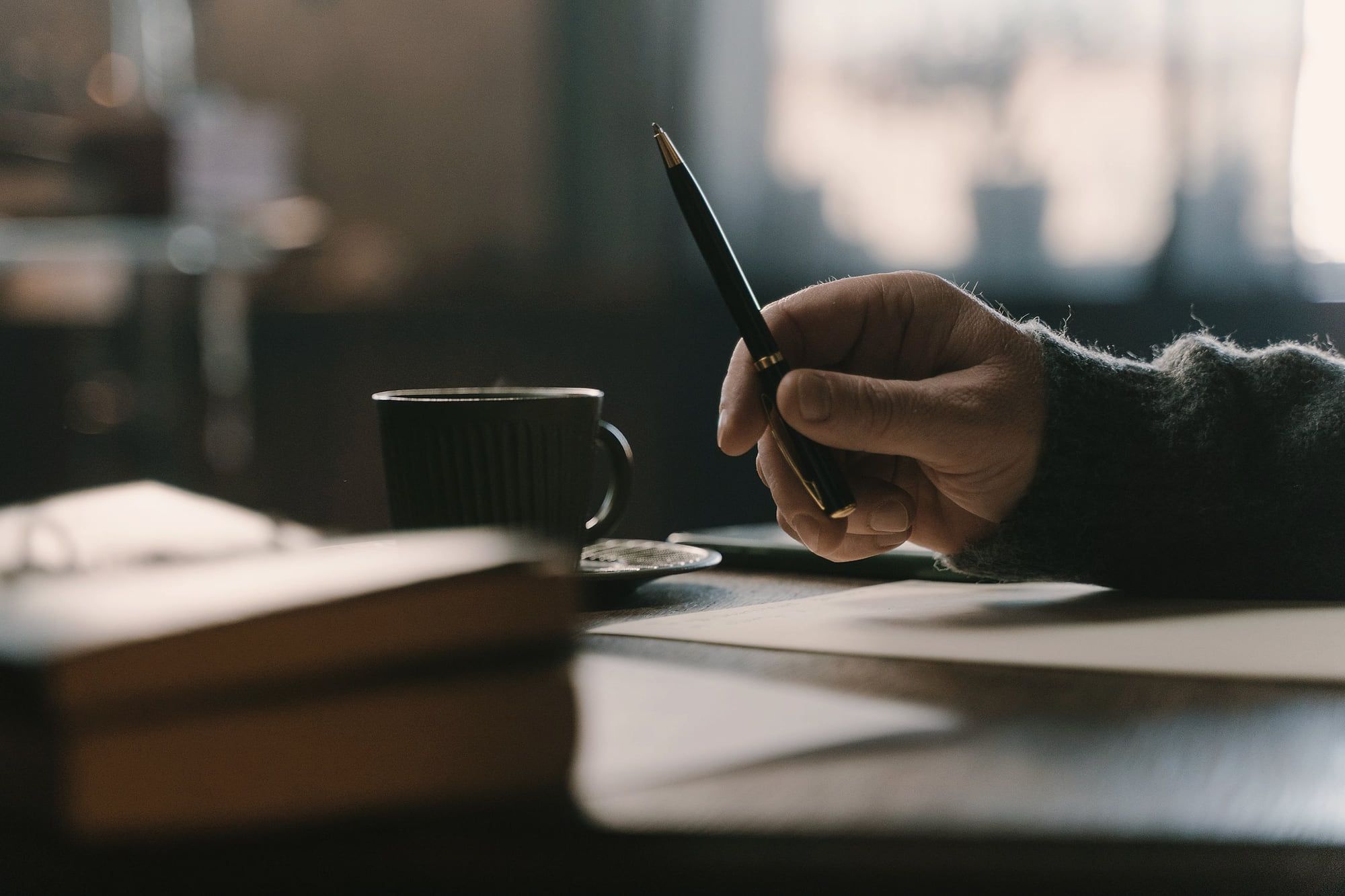 Une main prend des notes à côté d’une tasse de café.