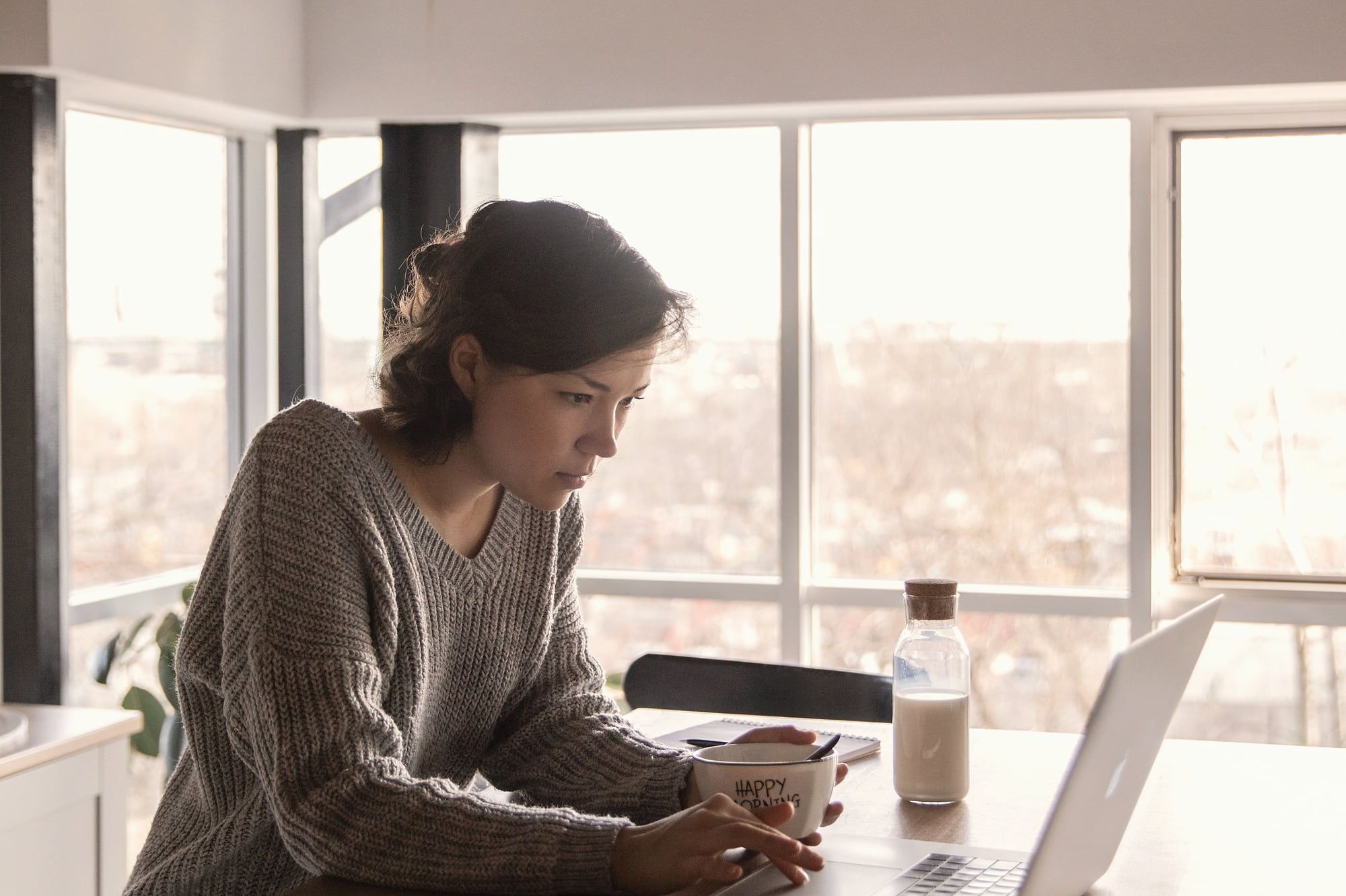 Une femme travaille à une table face à une grande baie vitrée.