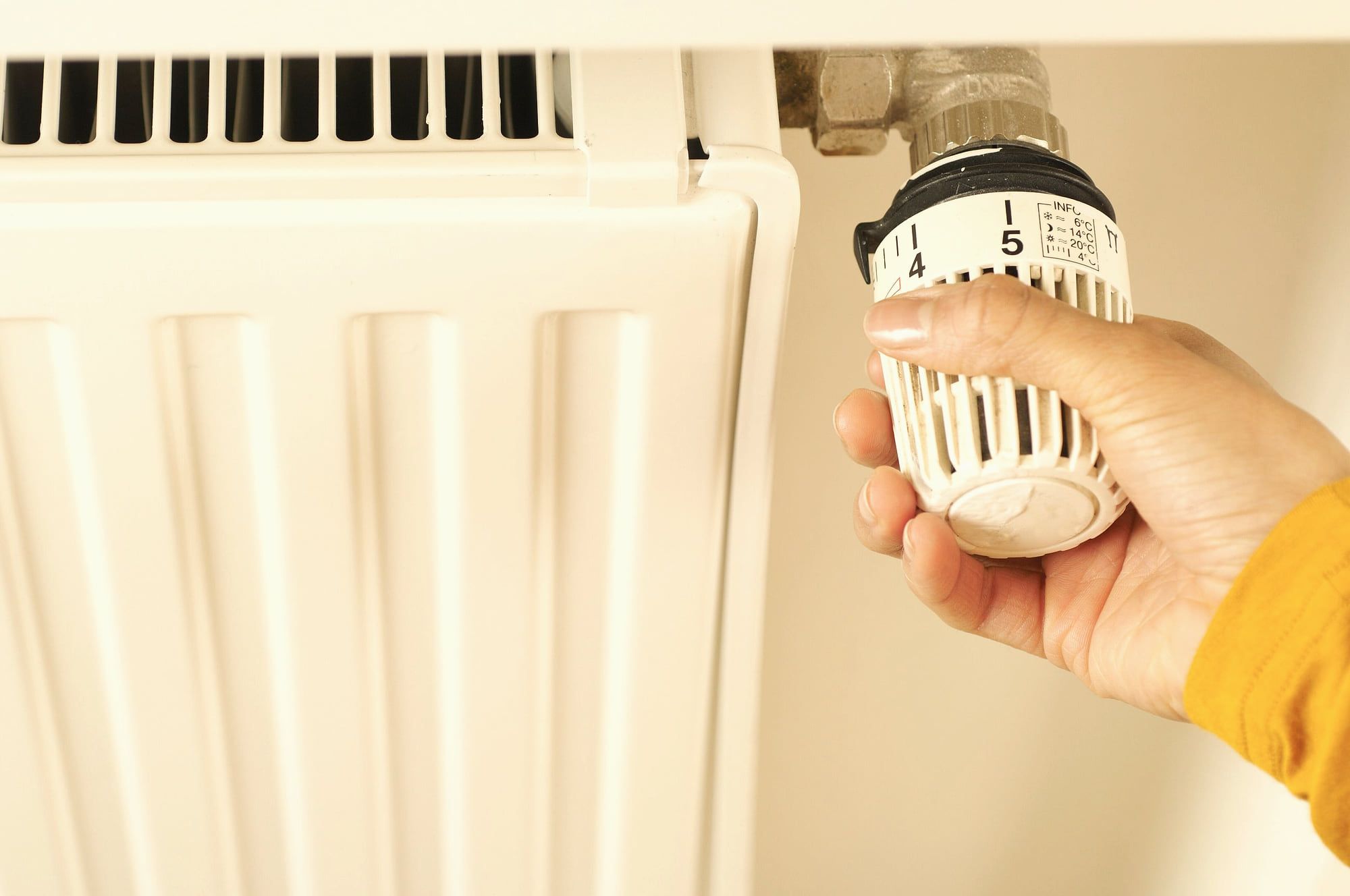 Une main règle le thermostat d’un radiateur.