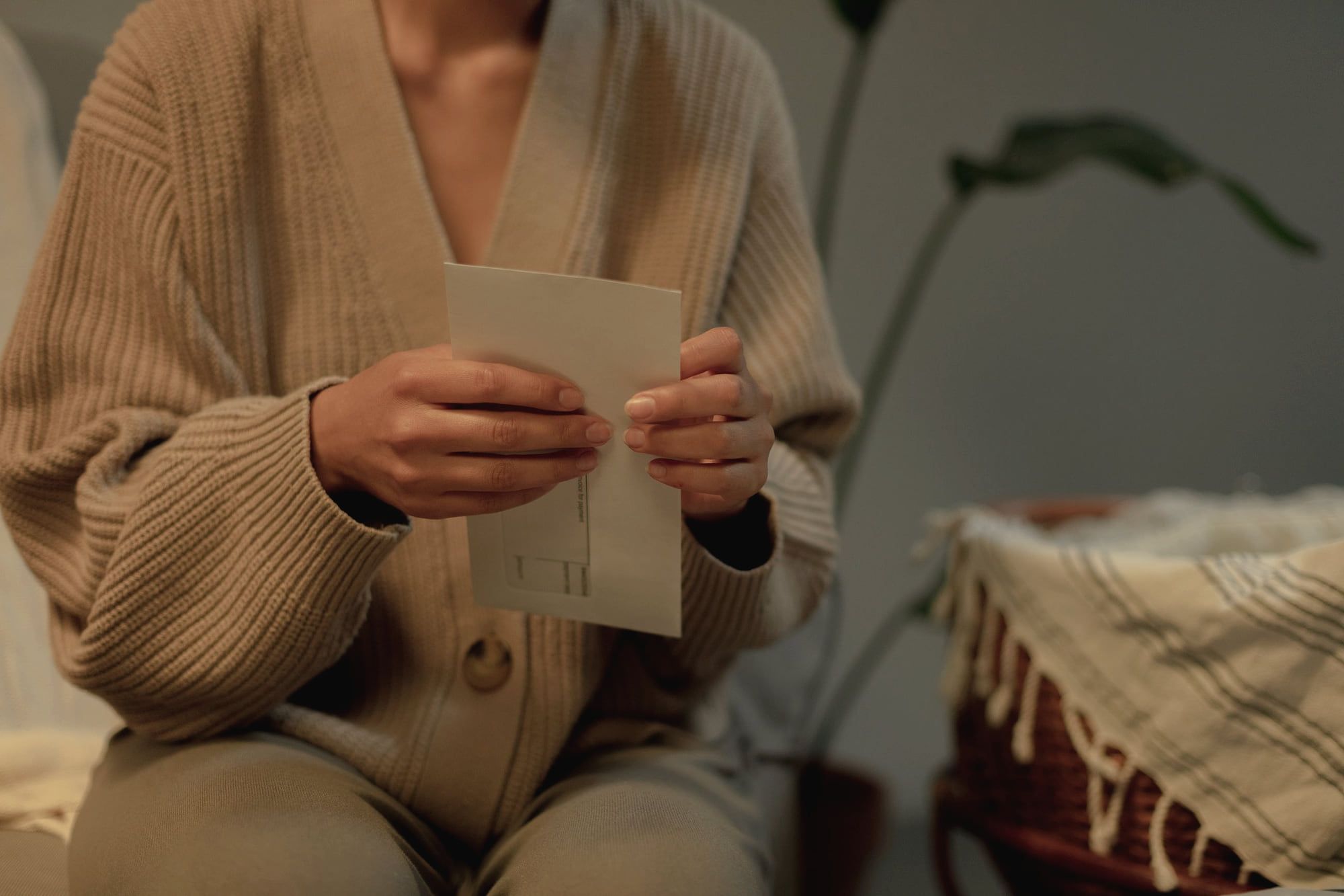 Une femme en gilet de laine tient une enveloppe entre ses mains.