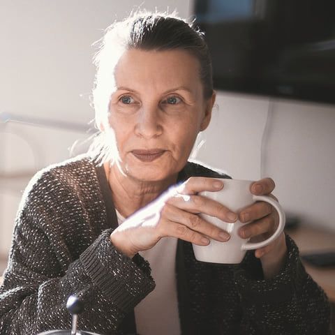 Une femme de 60 ans boit un café.