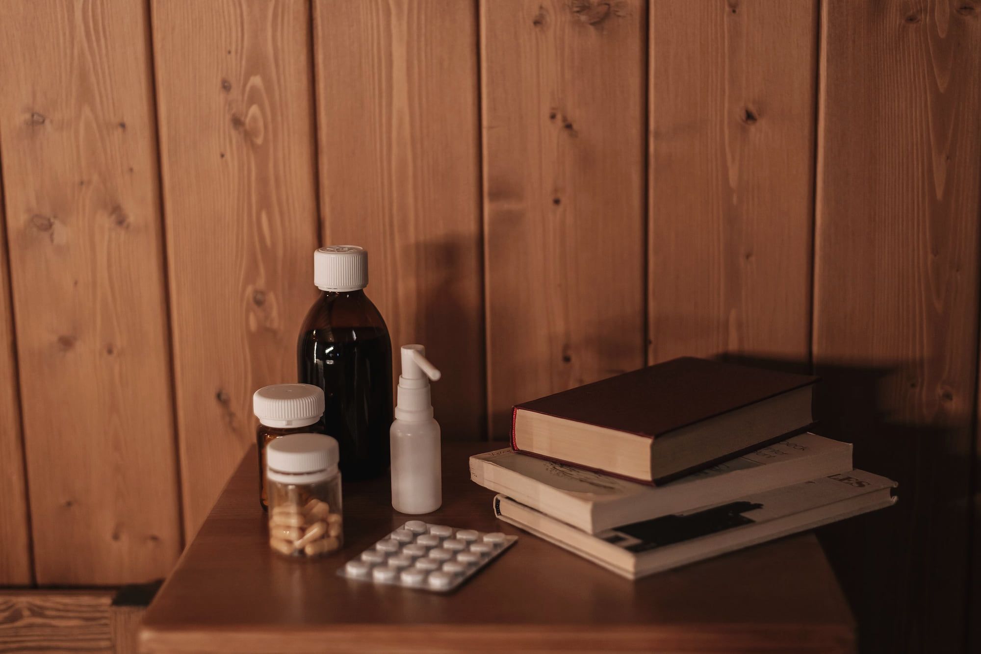 Des médicaments et des livres sur une table de chevet en bois.